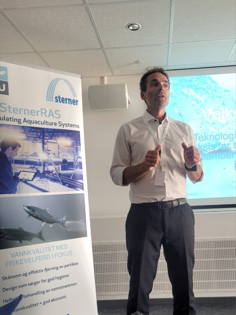 Stian Johnsen holder presentasjon foran en skjerm og en plakat med Sterner-logo og informasjon om vannkvalitet i fiskeoppdrett.